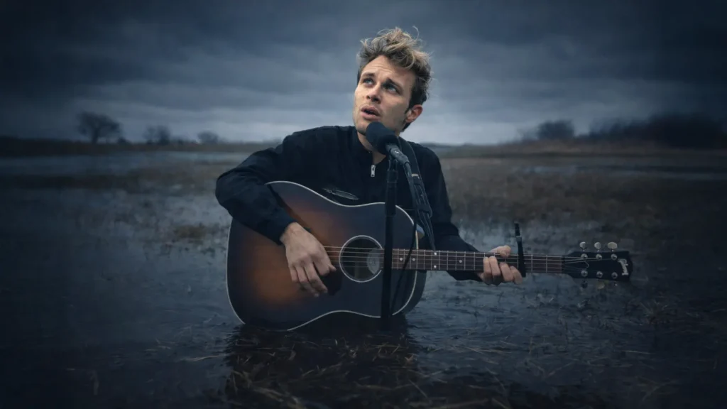 MUNE avec sa guitare le corps à moitié immergé dans l'eau lors d'un live de Après l'orage en zone inondée